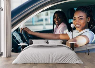 Two african young women on car trip driving the car and making fun. Wall mural